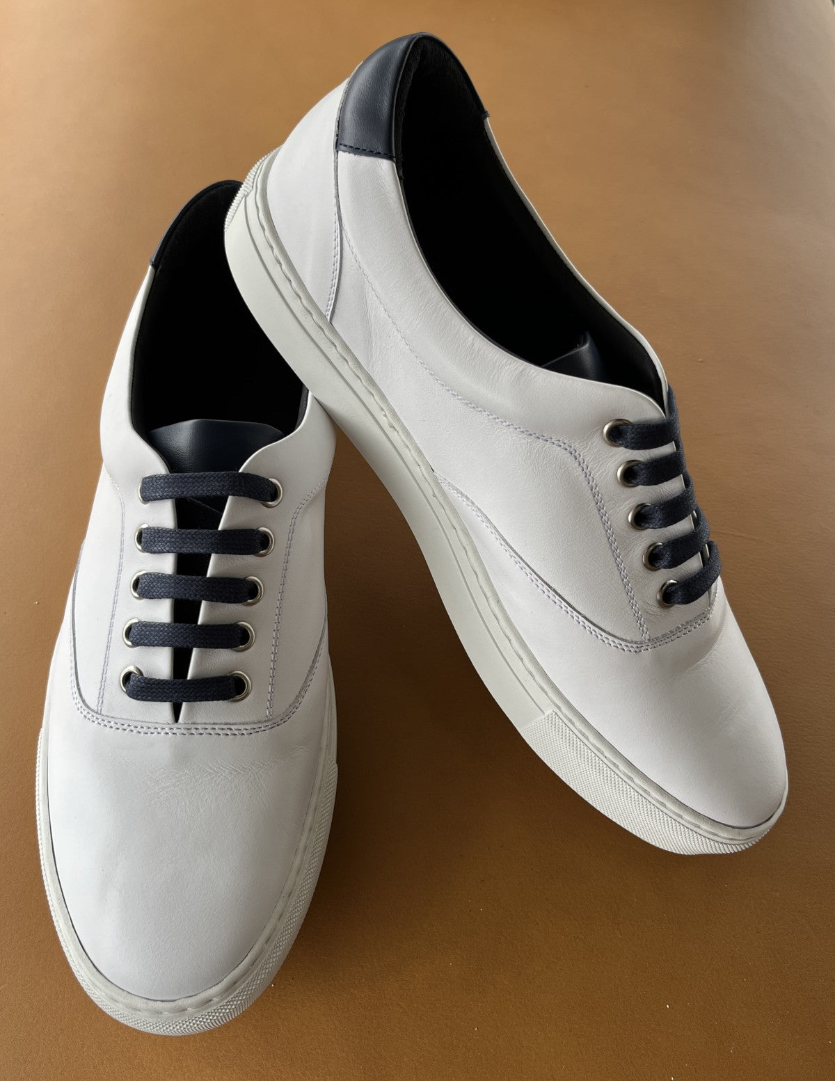 Add style to your favorite outfit with a cool soft leather sneaker in white with navy accent leather on the tongue and back heel.  Soft foot bed for a comfortable feel and clean style. Firm sole for structure and comfort. Perfect for around the town or at the office.  Classic fit and hand made in Spain. By Marcello Sport