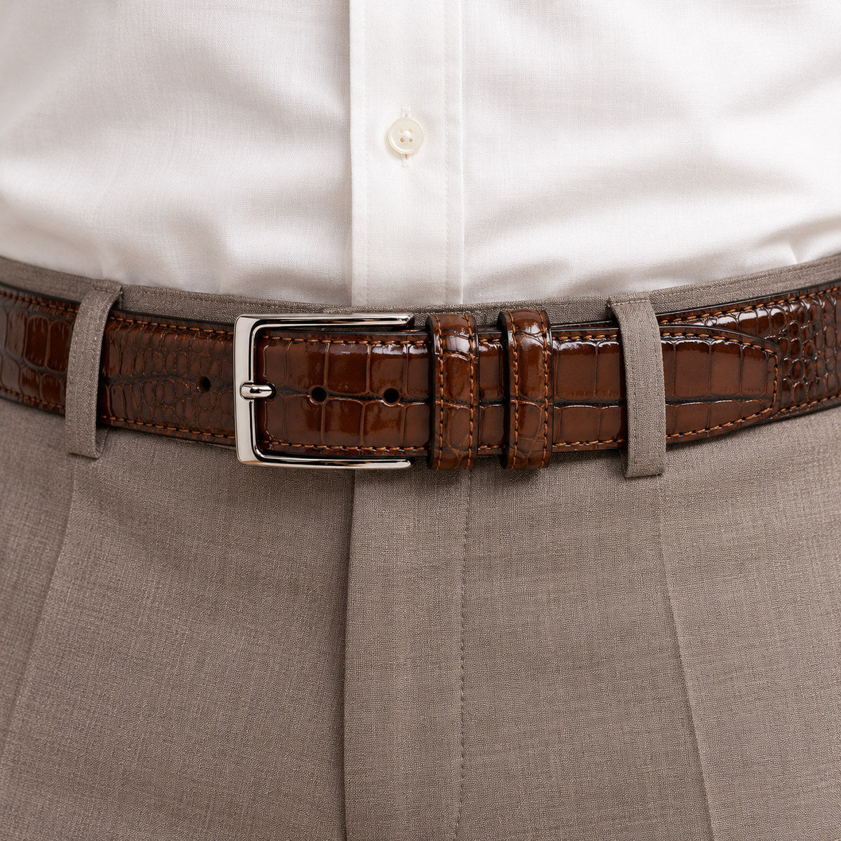 A Marcello Mocha Brown crocodile-embossed leather belt with a silver-tone metal buckle, coiled on a plain white background.