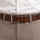 A Marcello Mocha Brown crocodile-embossed leather belt with a silver-tone metal buckle, coiled on a plain white background.