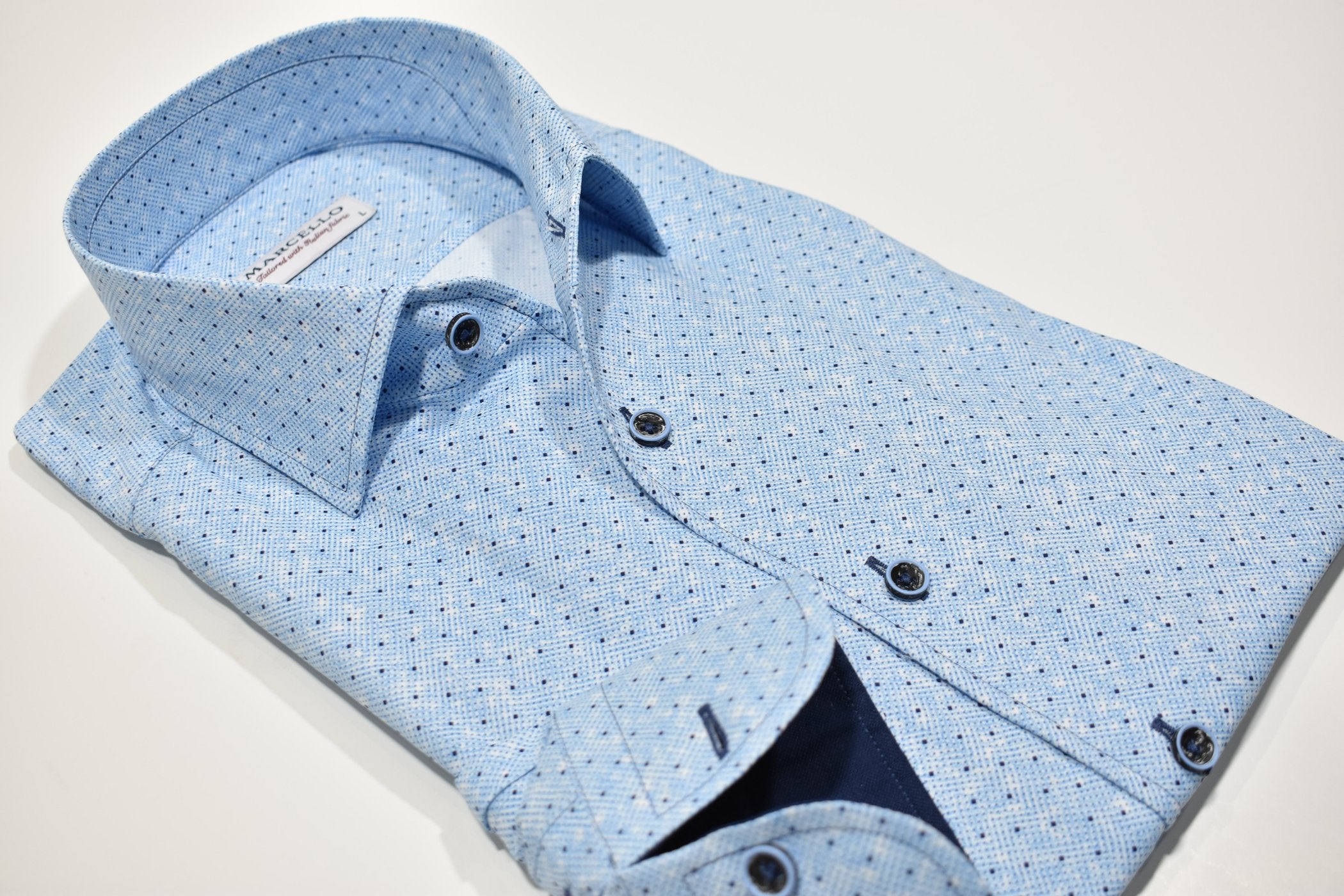 Elevate your style with the W932R Sky Dot Roll Collar. Featuring a Marcello exclusive one piece roll collar, this medium blue patterned herringbone shirt is accented with random navy dots. Exude confidence and sophistication with this must-have piece. By Marcello
