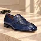 Robbie indigo gator-pattern penny loafer staged with black sunglasses on pale stone.