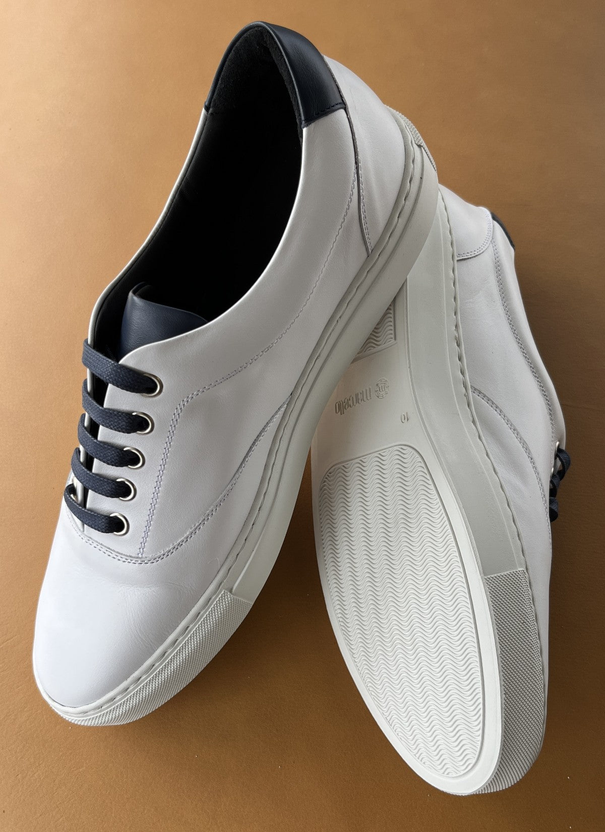 Add style to your favorite outfit with a cool soft leather sneaker in white with navy accent leather on the tongue and back heel.  Soft foot bed for a comfortable feel and clean style. Firm sole for structure and comfort. Perfect for around the town or at the office.  Classic fit and hand made in Spain. By Marcello Sport